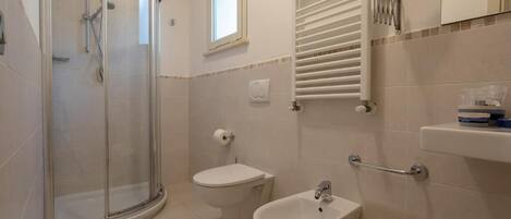 A bathroom with a glass-enclosed shower, a toilet, a bidet, and a sink.