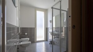 A modern bathroom with a toilet, bidet, and sink, a glass shower enclosure, and a visible toilet paper dispenser. - Hotel gimmi (Rimini)