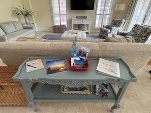 Ein Wohnzimmer mit einer Couch, einem Couchtisch mit Zeitschriften und einer Wasserflasche sowie einem Fernseher an der Wand.