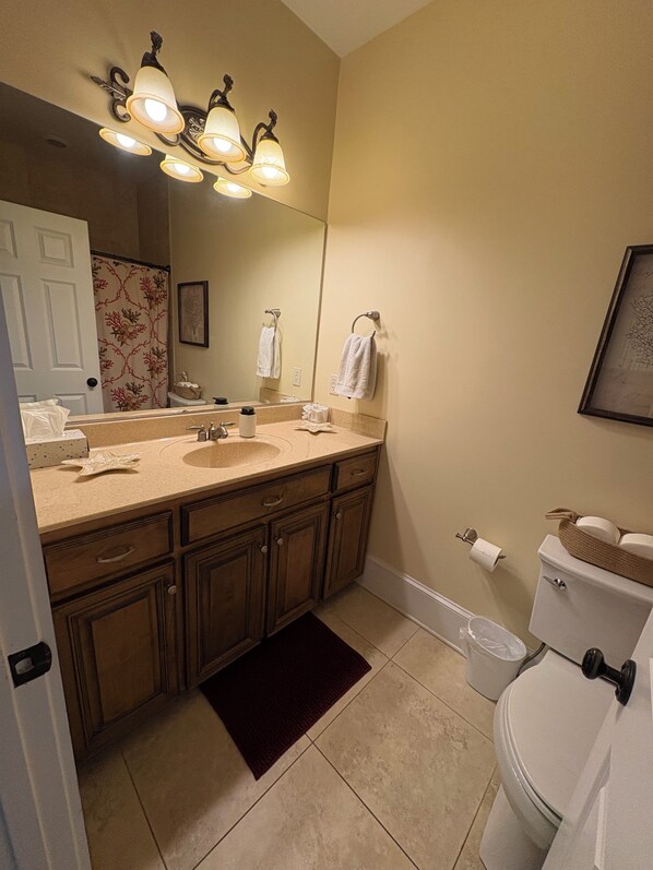 A bathroom with a vanity, sink, mirror, towel rack, toilet, and a trash can. - Beautiful, beachfront, 2 bedroom condo with ocean-front pool! (St. Simons Island)