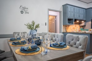 Una mesa de comedor decorada con servilletas azules, platos y vasos, una planta en maceta, y un letrero en la pared que dice 'Coffee and Tea'.