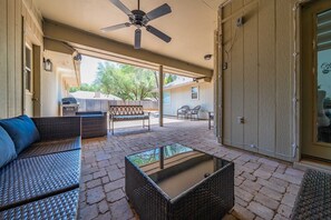 An outdoor patio with wicker furniture, a ceiling fan, and a glass-top coffee table.
