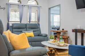 Una sala de estar moderna con un sofá gris, cojines amarillos, una mesa de centro con aperitivos y una planta pequeña.