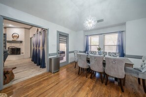 Un coin repas avec une table dressée pour quatre personnes, un lustre moderne et une vue sur l’espace de vie, accessible par une porte vitrée.