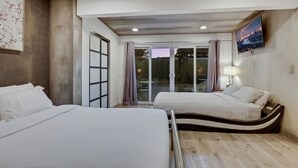 Hotelkamer met twee bedden, een schuifdeur naar een balkon, een flatscreen televisie en een schilderij aan de muur.