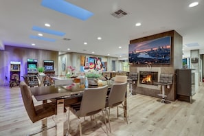 A modern living room with a dining area, a fireplace, and a cityscape painting. - Luxury Vegas Compound: Waterfall Pool & Full Court (Las Vegas)
