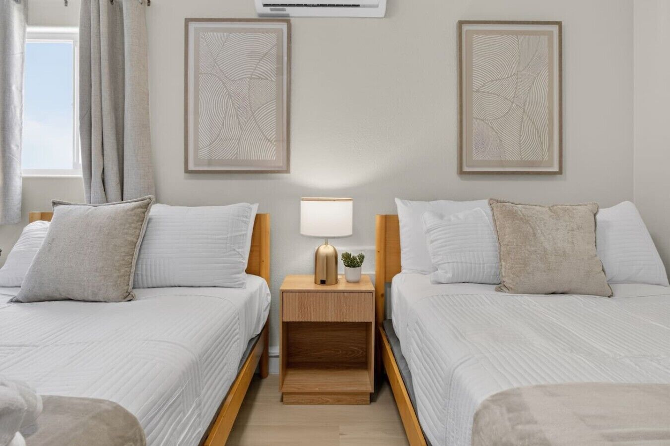 Une chambre double avec deux lits, une table de chevet avec une lampe et deux œuvres d’art encadrées accrochées au mur.