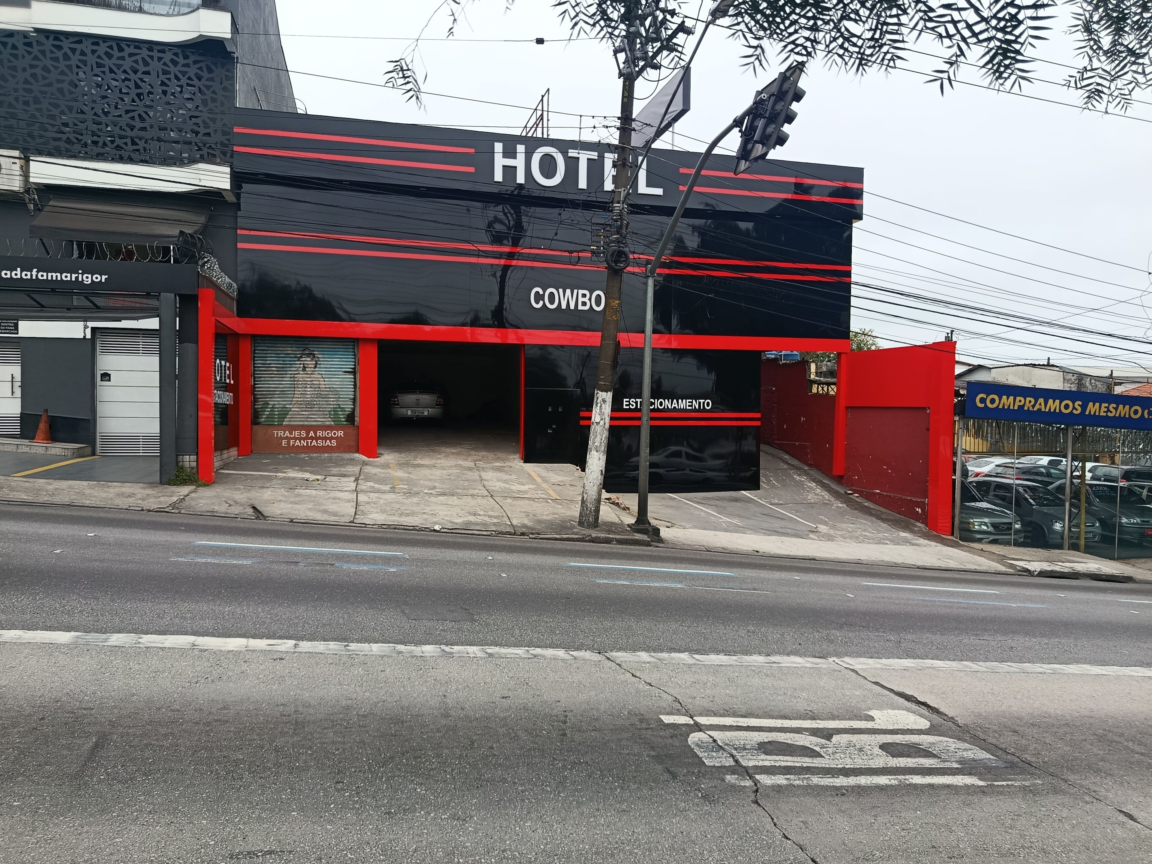 A hotel with a black facade and red accents, a visible entrance, and a parking area with cars.