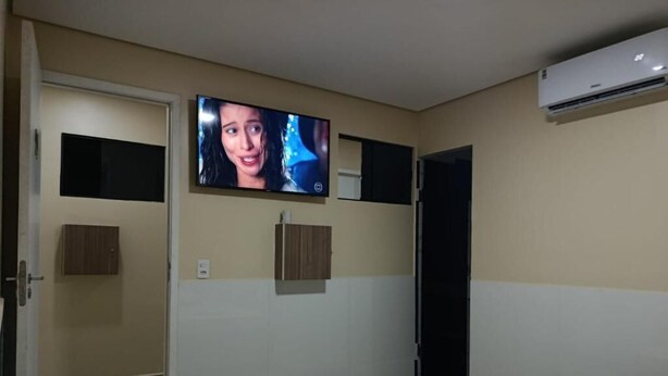 Habitación de hotel con cama, televisión, aire acondicionado instalado en la pared y una puerta que da a otra habitación.
