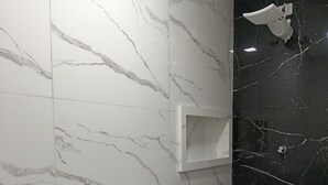 Un baño con paredes de mármol blanco, una pared de acento en mármol negro, un inodoro blanco y una zona de ducha.