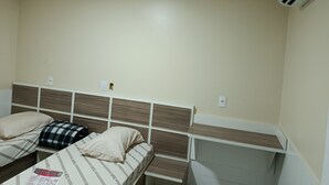 Habitación de hotel con dos camas, cabecera con diseño de rejilla, aire acondicionado de pared y una pequeña estantería.