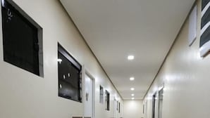 Un pasillo largo y estrecho con puertas a ambos lados, iluminación empotrada y un suelo de baldosas brillantes.