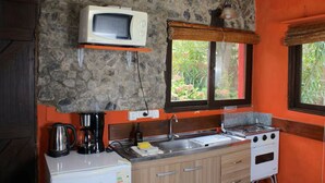Una cocina con pared de piedra, microondas, estufa, cafetera y ventana con vista a zonas verdes.