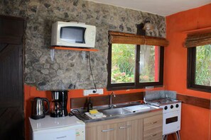 A kitchen with a stone wall, a microwave, a stove, a coffee maker, and a window with a view of greenery.