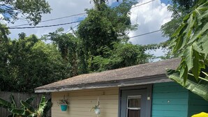 A residential house with a small porch, a potted plant, and a wicker chair. - Cozy 1-bedroom studio tiny home experience (Orlando)