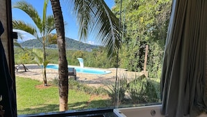 Una habitación con una bañera grande, vistas a una piscina y un entorno tropical al aire libre.