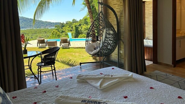 Un dormitorio con cama, una silla colgante, una mesa y vistas a una piscina y follaje.
