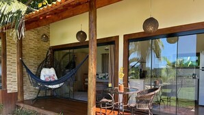 Una terraza de madera con una hamaca, sillas de mimbre y una mesa con un jarrón de flores.