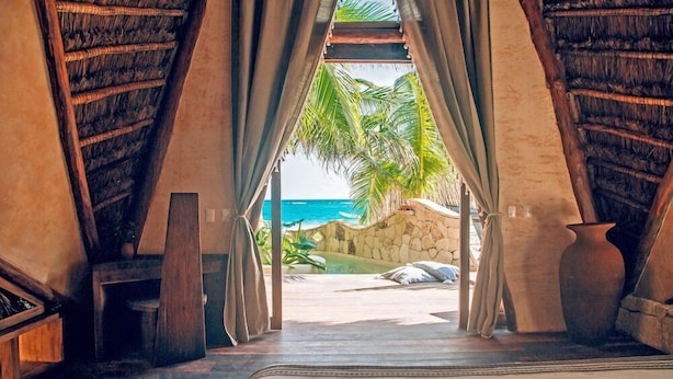 Una habitación con cama, cortinas, pared de piedra y vista a la playa.