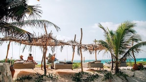 Una playa con estructuras de techo de paja, sillas de descanso y palmeras.