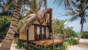 Una casa de playa con techo de paja, terraza de madera y rodeada de palmeras.