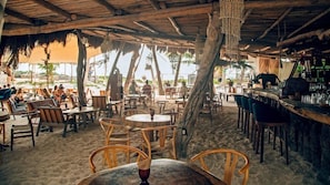 Restaurante ao ar livre com mobiliário de madeira, área de bar e vista para a praia.