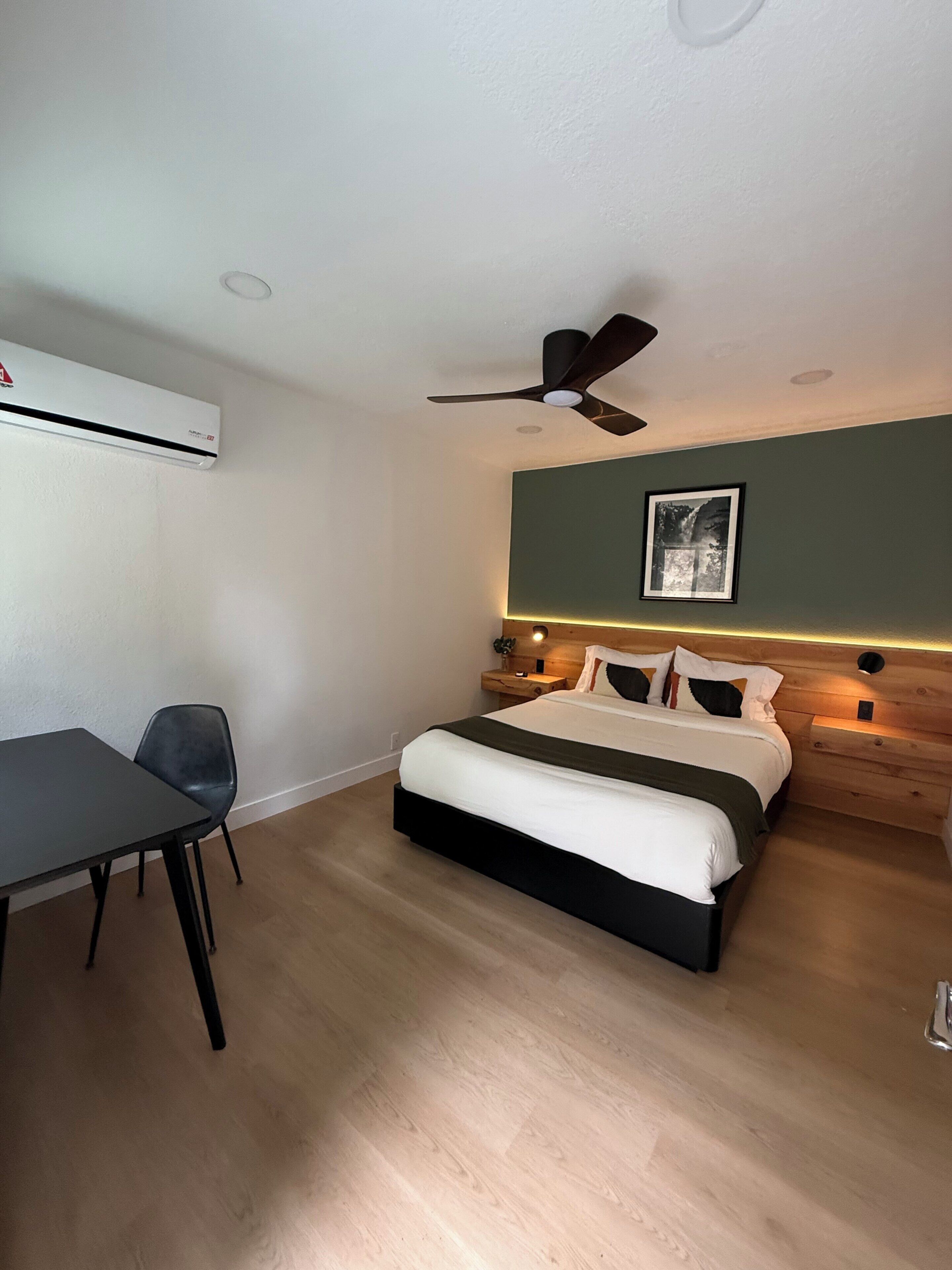 A bedroom with a bed, a desk, a chair, a ceiling fan, and a wall-mounted air conditioner.