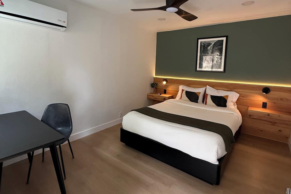 A bedroom with a bed, a desk, a chair, a ceiling fan, and a wall-mounted air conditioner.