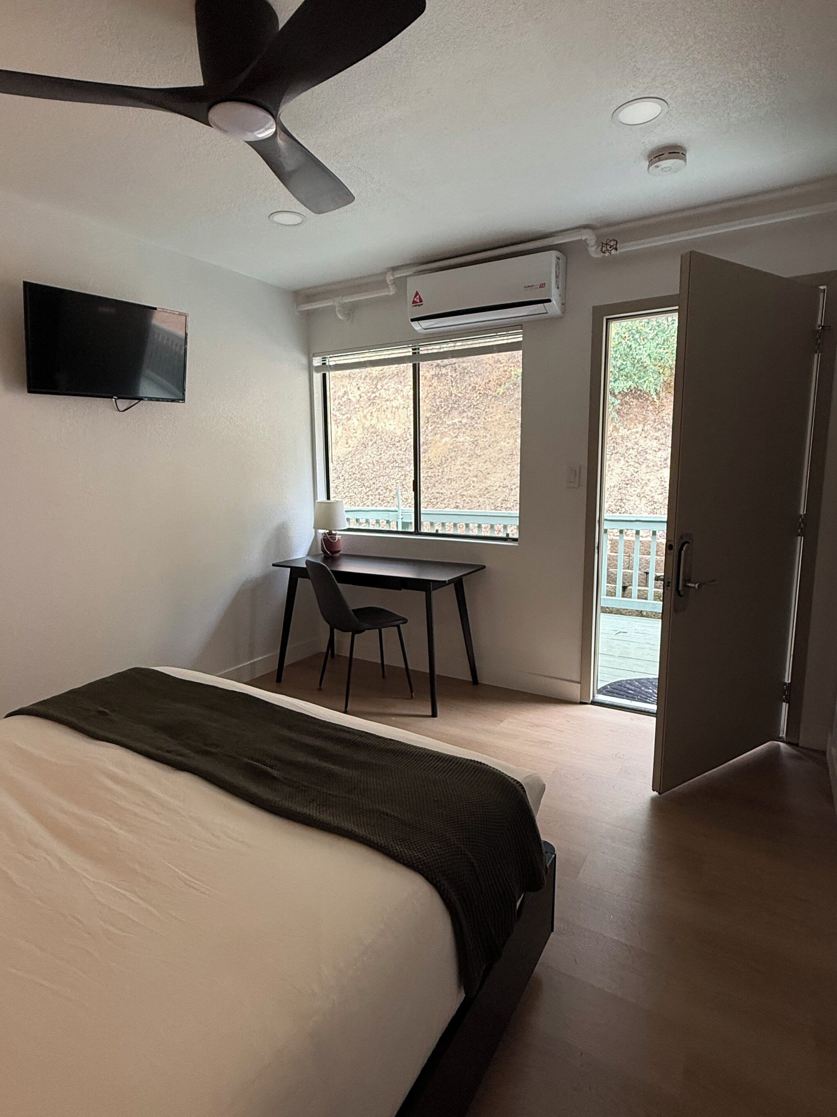 A bedroom with a bed, a desk, a chair, a television, and a ceiling fan.