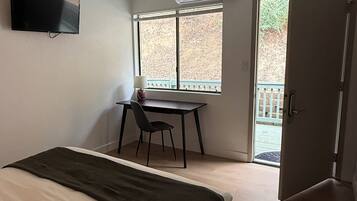 A bedroom with a bed, a desk, a chair, a television, and a ceiling fan.