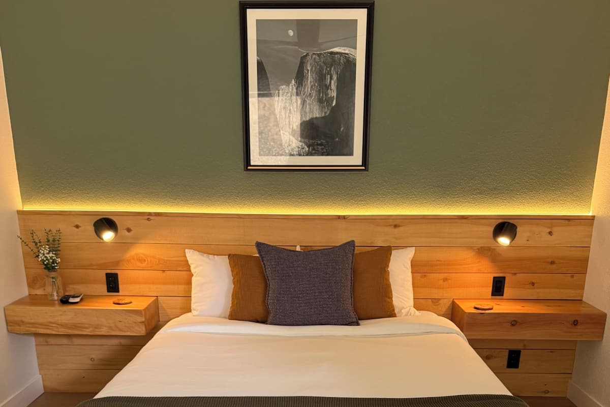 A modern bedroom with a large bed, wooden headboard, bedside tables, and a framed picture on the wall.