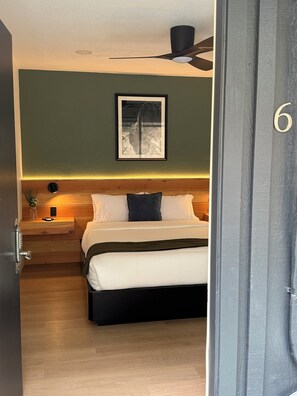 A bedroom with a bed, a nightstand, a framed picture on the wall, a ceiling fan, and a door with a number. - Granite Ridge (Oakhurst)