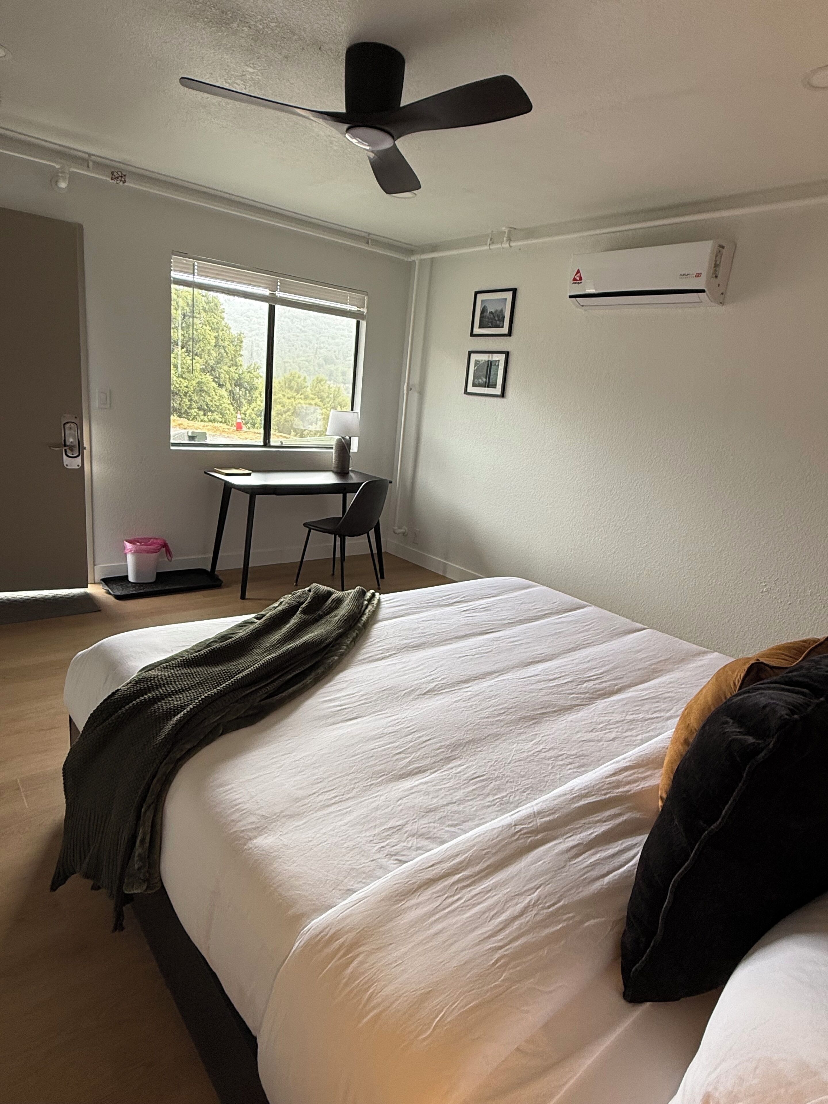 Un dormitorio con cama, escritorio, silla, ventana y ventilador de techo.