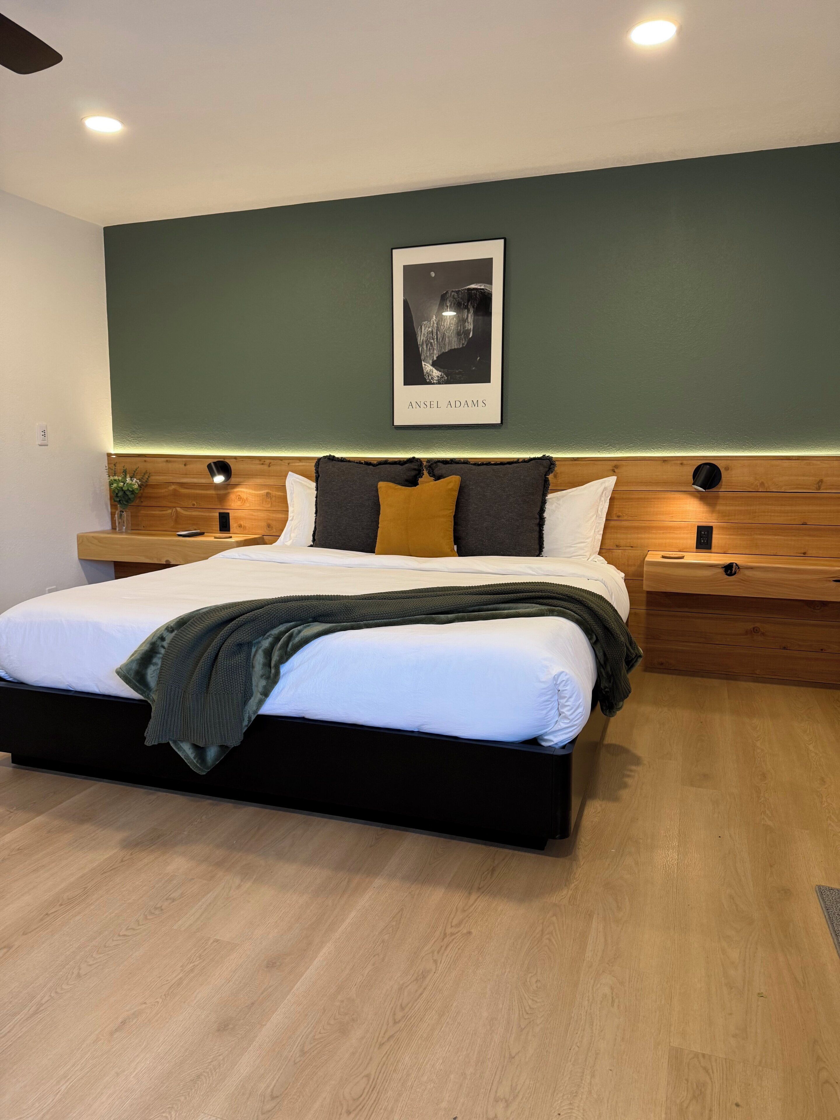 A modern bedroom with a bed, bedside tables, a nightstand, a framed picture, and a ceiling fan.