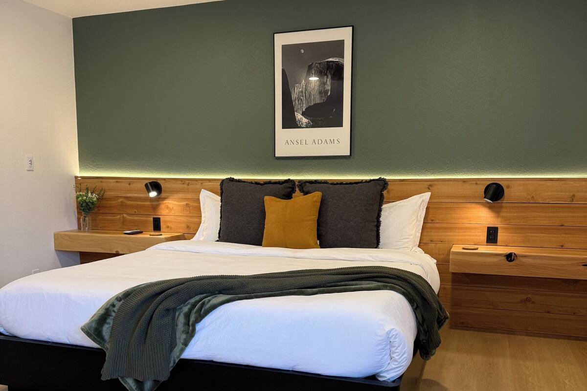 A modern bedroom with a bed, bedside tables, a nightstand, a framed picture, and a ceiling fan.