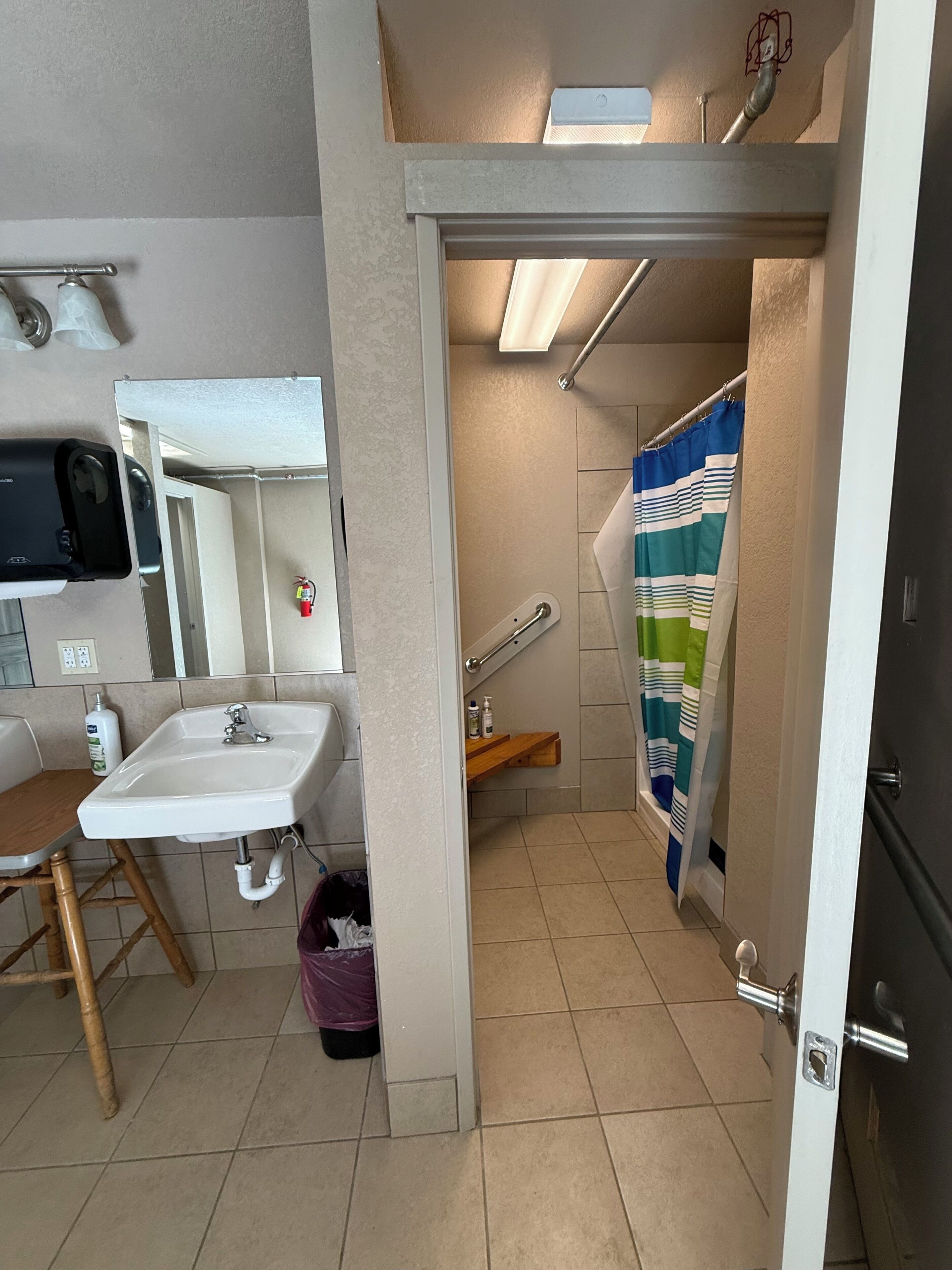 Un baño con lavamanos, espejo, cortina de ducha y una silla de madera.