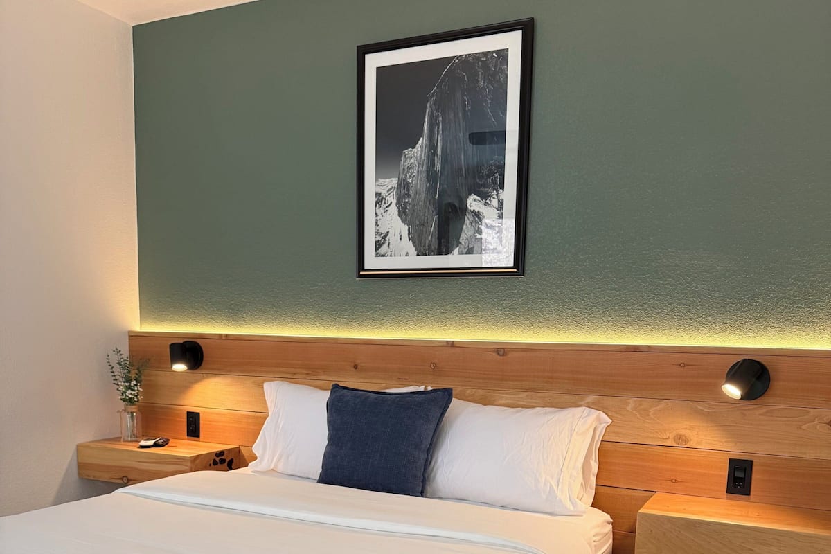 A neatly arranged bedroom with a bed, wooden headboard, bedside tables, and a framed picture on the wall.