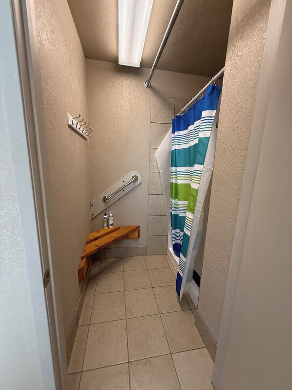 A small bathroom with a shower curtain, a towel rack, a wooden shelf, and a hand dryer. - Granite Ridge (Oakhurst)
