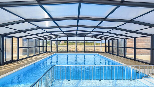Une piscine intérieure dotée d’un toit en verre, entourée de rampes de protection en métal.