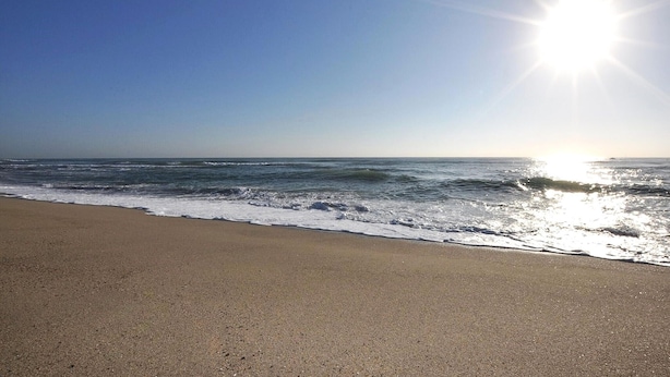 Una playa con olas, cielo despejado y sol brillante.