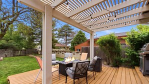Un patio al aire libre techado con una mesa de fogata, sillas y una parrilla.