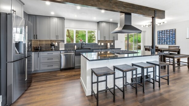 Una cocina moderna con armarios grises, electrodomésticos de acero inoxidable y una isla central con taburetes de bar.
