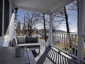 Eine überdachte Veranda mit weißer Brüstung, einem grauen Sofa und einem Tisch mit weißer Tasse.