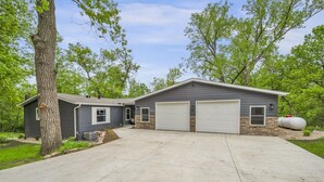 Ein zweistöckiges Haus mit Garage, kleiner Werkstatt und einem großen Baum davor.