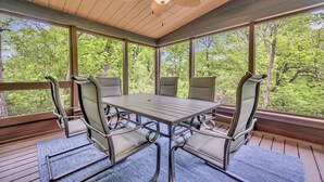 Eine überdachte Terrasse mit Tisch und Stühlen, großen Fenstern und einem Deckenventilator.