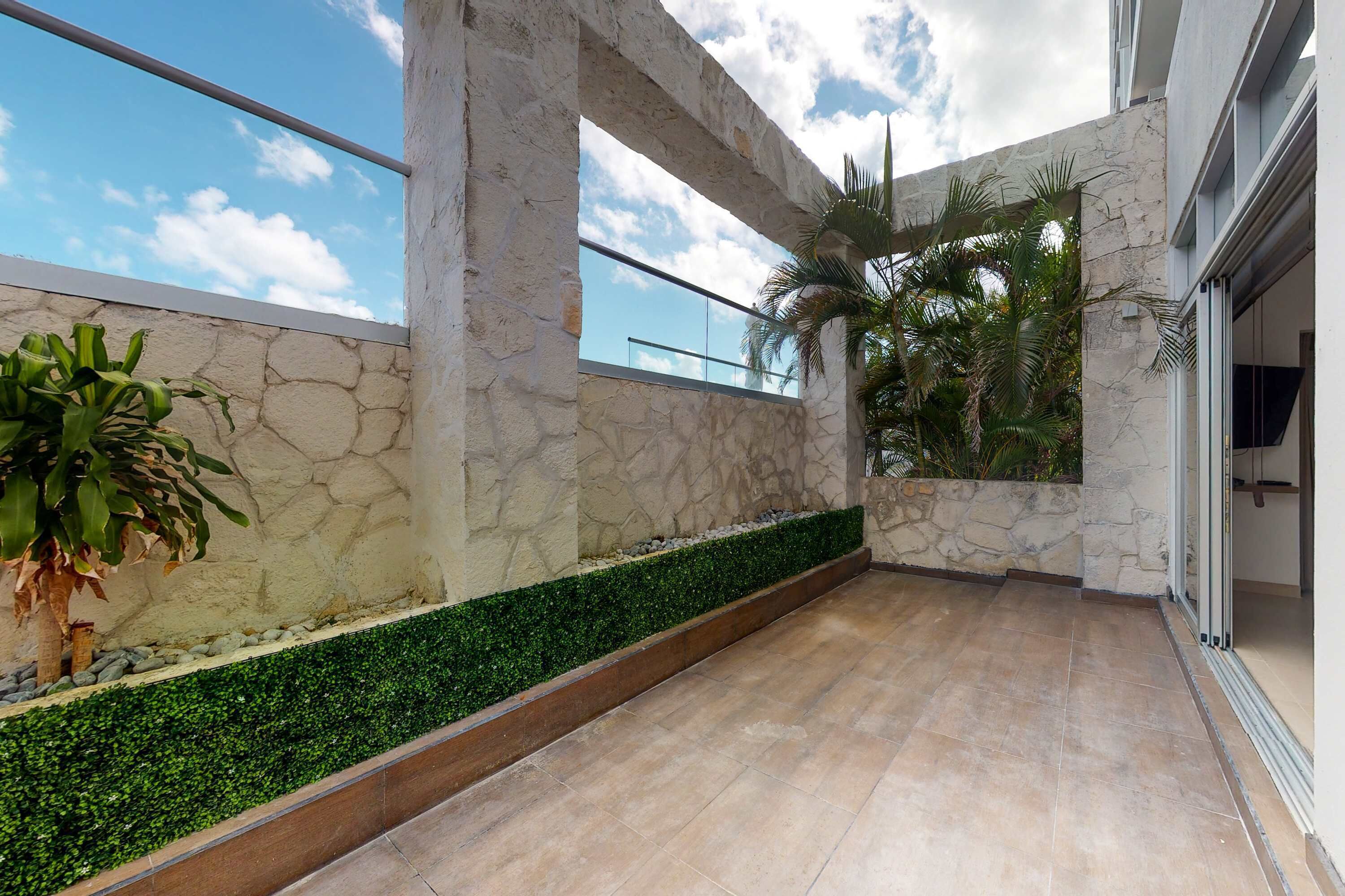 A modern building with stone walls, a green hedge, and a tiled floor.