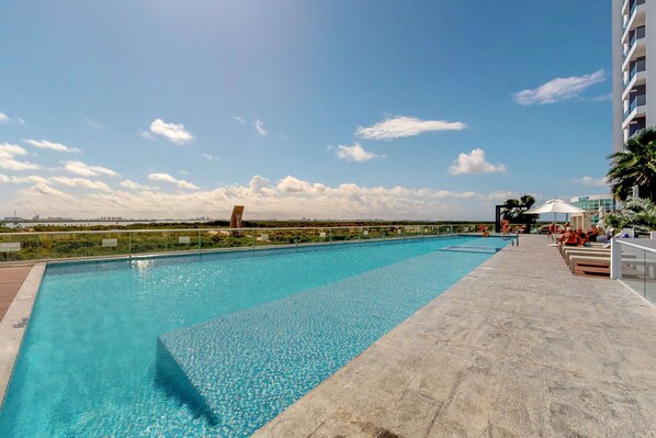 A swimming pool with a clear sky and distant buildings. - Cancun Malecon 2BR/2BA | Pool, Gym & Terrace (Cancún)