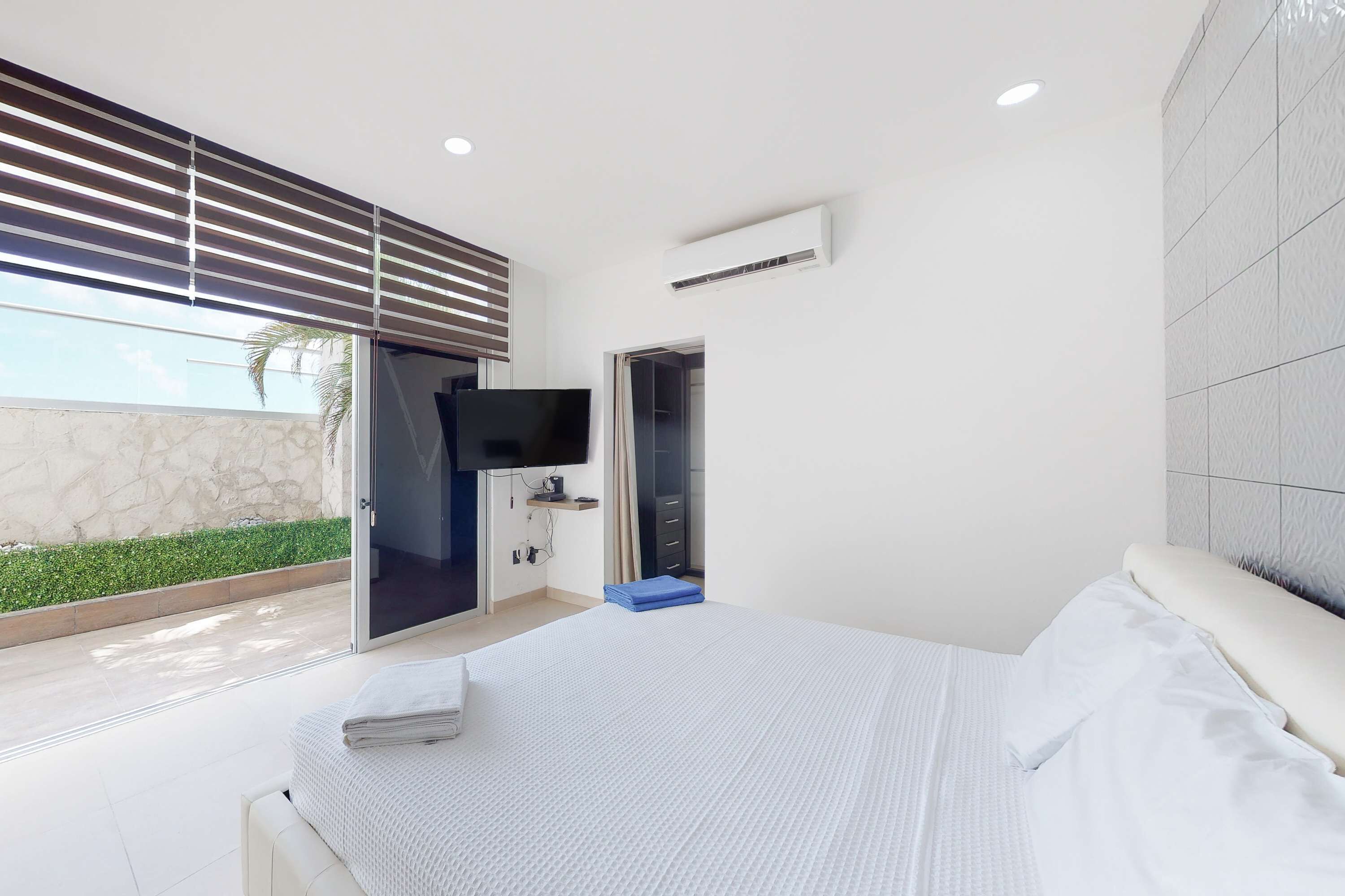 A modern bedroom with a large bed, a TV, and a sliding door leading to a balcony.