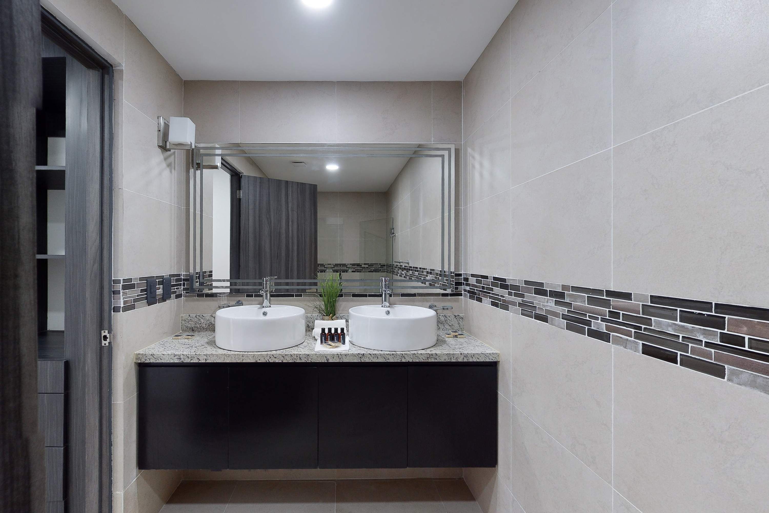 Casa de banho com duas pias, espelho e painel de azulejos.