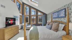 Ein Schlafzimmer mit Bett, Fernseher, Kommode und großen Fenstern.